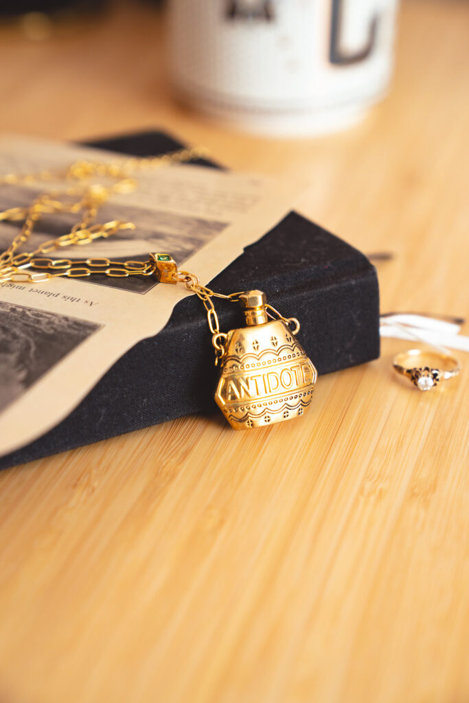 A tiny antidote bottle on a gold chain on Cassie's desk.